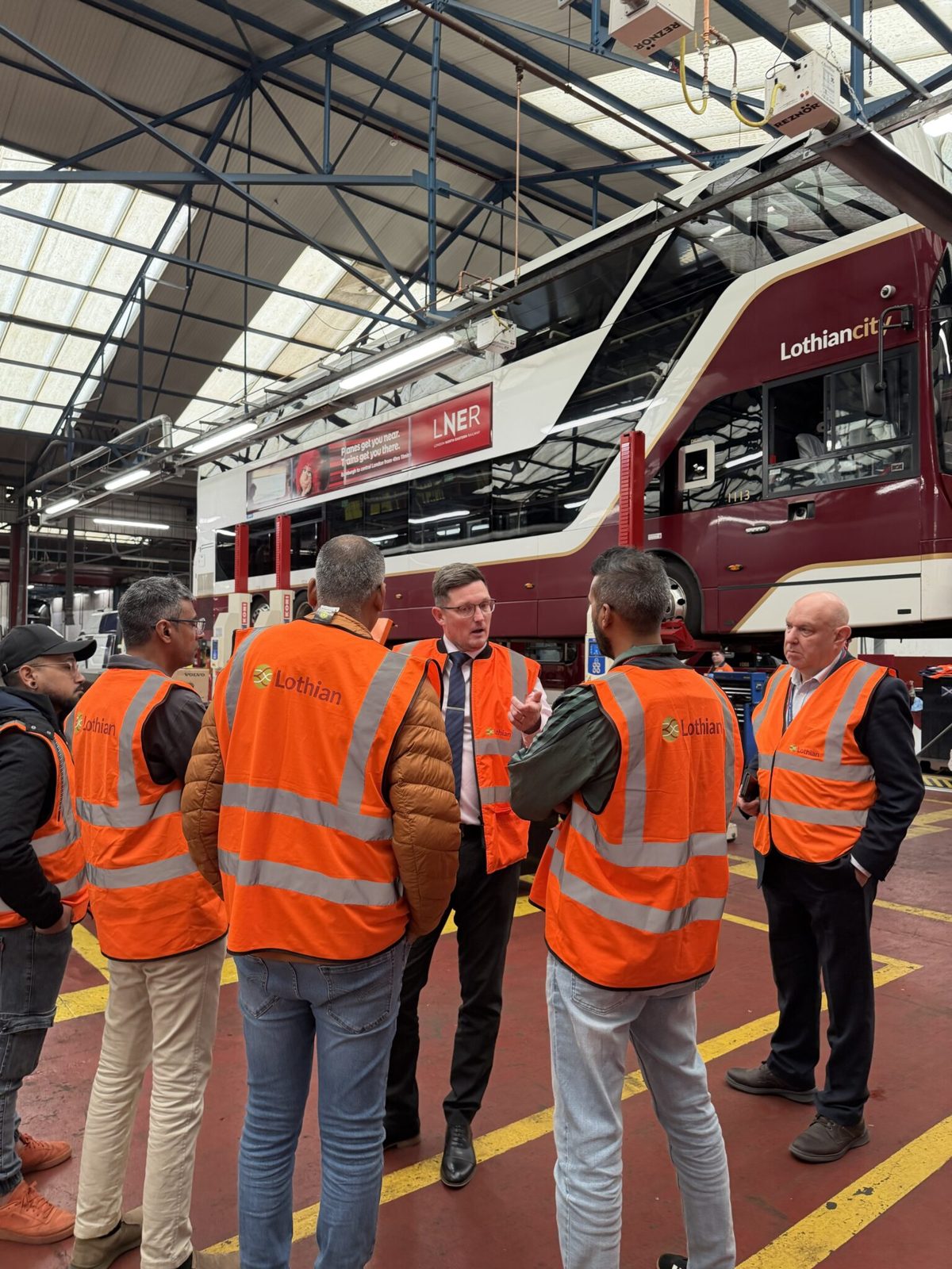 Group in hi-vis vests beside an electric bus in a maintenance depot